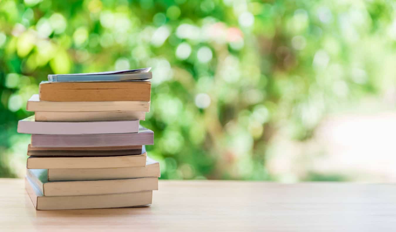 A stack of books on a  table outside on a sunny day