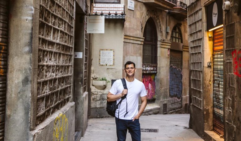 Nomadic Matt with a backpack slung over his shoulder, walking through the narrow streets of the Gothic Quarter in Barcelona, Spain