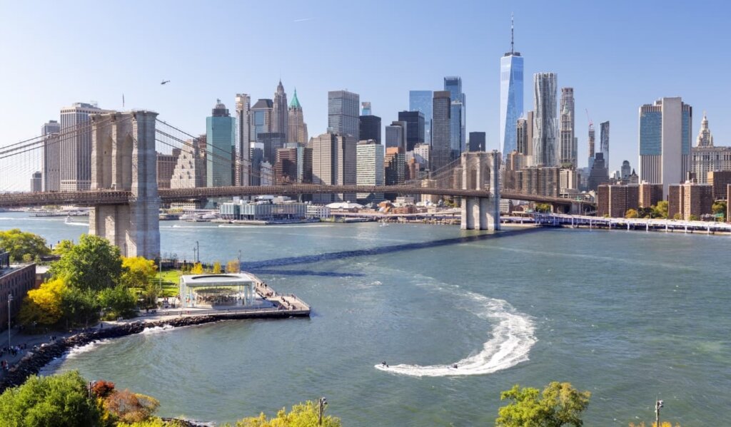 Panoramic view of the Manhattan skyline across the East River with the Brooklyn Bridge in the foreground